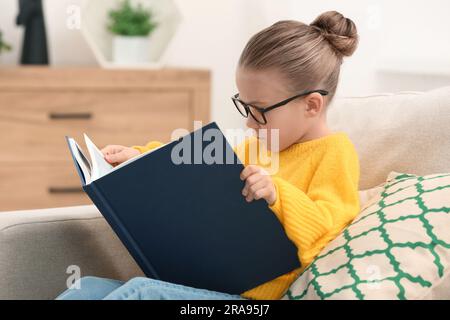 Süßes kleines Mädchen mit Brille, das drinnen Buch liest Stockfoto