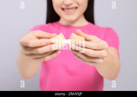 Junge Frau mit leckerem Glückskeks, mit Vorhersage auf grauem Hintergrund, Nahaufnahme Stockfoto