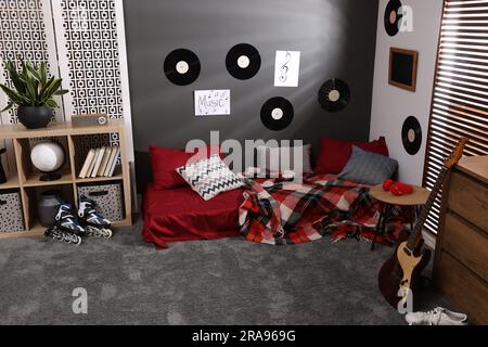 Stilvolles Teenagerzimmer mit Bett, Gitarre und Schallplatten an der Wand. Innendesign Stockfoto