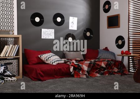 Stilvolles Teenagerzimmer mit Bett, Holztisch und Vinylplatten an der Wand. Innendesign Stockfoto