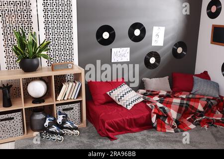 Stilvolles Teenagerzimmer mit Bett, Holzständer und Schallplatten an der Wand. Innendesign Stockfoto