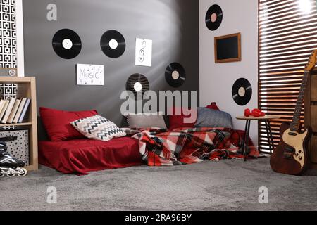 Stilvolles Teenagerzimmer mit Bett, Gitarre und Schallplatten an der Wand. Innendesign Stockfoto