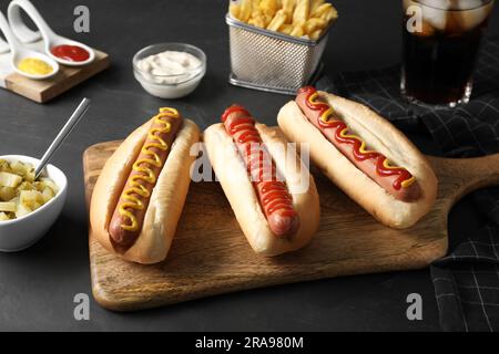 Frische, köstliche Hot Dogs mit Saucen, serviert auf einem schwarzen Tisch Stockfoto