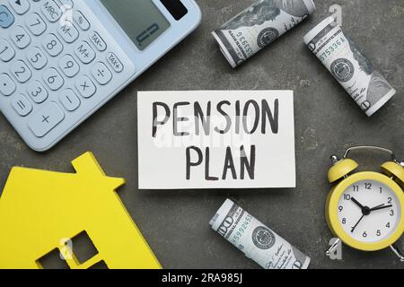 Karte mit Wörtern Pensionsplan, Taschenrechner, Hausfigur, Wecker und Dollarscheine auf grauem Tisch, flach liegend Stockfoto