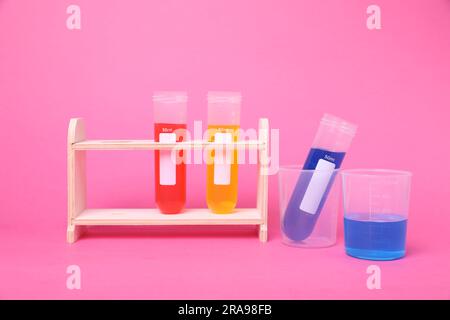 Bechergläser und Reagenzgläser mit bunten Flüssigkeiten in einem Holzständer auf hellem pinkfarbenen Hintergrund. Chemie-Experiment-Set für Kinder Stockfoto