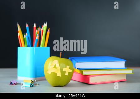 Apfel mit geschnitztem Buchstaben A und Pluszeichen als Sorte. Schulpapier auf weißem Tisch im Klassenzimmer, Platz für Text Stockfoto