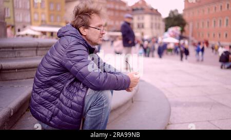 Ein erwachsener Mann sitzt auf dem Platz und raucht eine Tabakpfeife auf dem Palastplatz, Warschauer Altstadt Stockfoto