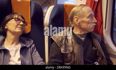 Ein älteres Paar reist im Zug, der Senior schaut aus dem Fenster, eine Frau schläft Stockfoto