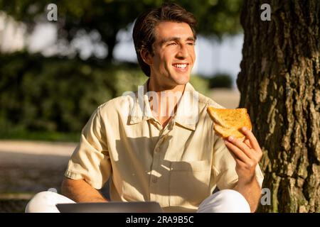 Porträt eines glücklichen jungen Mannes, der Sandwich im Park isst Stockfoto