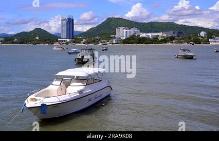 Hügel- und Hochhäuser in der Ferne, Boot im Vordergrund, in der Stadt Si Racha, an der Küste des Bezirks Si Racha, Provinz Chonburi, Thailand. Foto von Koh Loy, einer kleinen schwimmenden Insel, die über eine Brücke von etwa 500 Metern Länge mit der Küste verbunden ist. Stockfoto