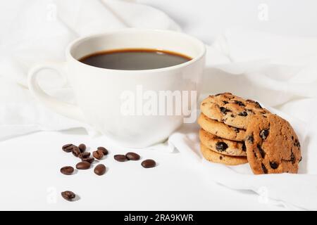 Große Tasse Kaffee am Morgen auf weißem Tuch mit Bohnen und Keksen Stockfoto