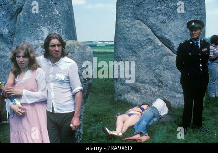Stonehenge Free Festival bei der Sommersonnenwende, Wiltshire, England, Juni 21. 1979. Neben den Hippies beobachtete eine kleine Gruppe englischer Touristen, wie andere in der Sonne lagen, und ein 'Wachmann' stand daneben. 1970S GB HOMER SYKES Stockfoto