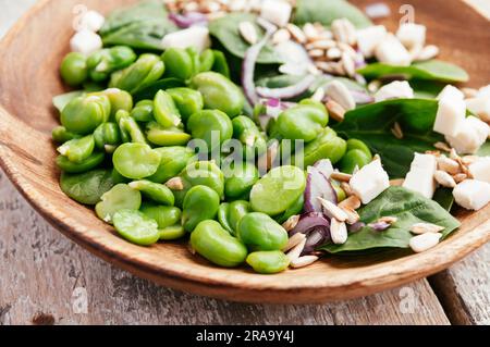 Ein frischer Salat mit geschälten Saubohnen, Baby-Blattspinat, roten Zwiebeln, Pinienkernen und zerbröckelte Soja-Käse. Stockfoto