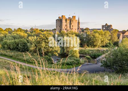 Blick über den Fluss Boyne in Richtung Trim Castle in der Grafschaft Meath, Irland, mit einer Fußgängerbrücke über dem Wasser. Stockfoto