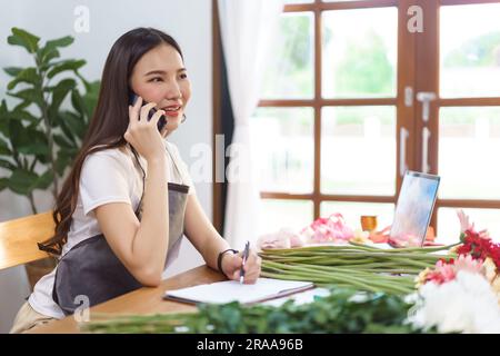 Blumengeschäft Konzept, weibliche Floristin im Gespräch mit dem Kunden auf dem Smartphone und notieren auf Notebook. Stockfoto