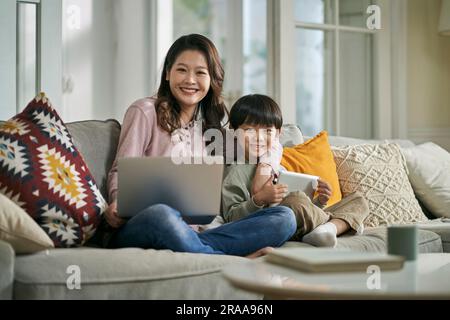 Wunderschöne asiatische Mutter und ein fünfjähriger Sohn, der zu Hause auf der Familientisch sitzt und die Kamera lächelt Stockfoto