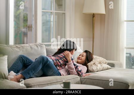 Junge asiatische Mutter, die auf der Couch der Familie liegt und sich von Angesicht zu Angesicht mit einer siebenjährigen Tochter unterhalten hat Stockfoto