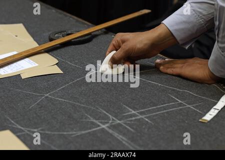 Schneiden Sie bei Anderson & Sheppard Bespoke in Savile Row, London, Großbritannien, ein markierendes Stoffmuster mit Kreide zu. Stockfoto