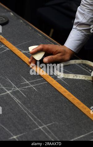 Schneiden Sie bei Anderson & Sheppard Bespoke in Savile Row, London, Großbritannien, ein markierendes Stoffmuster mit Kreide zu. Stockfoto