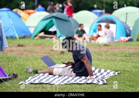 Ein Zuschauer auf seinem Laptop, während er sich über Nacht in der Schlange vor den Meisterschaften befindet, die am Montag beginnen. Foto: Sonntag, 2. Juli 2023. Stockfoto