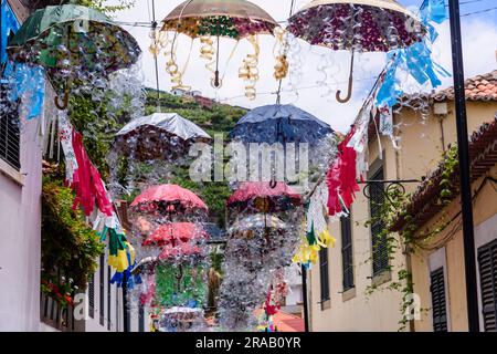 Kunstwerke aus Dutzenden von mehrfarbigen Regenschirmen, die über einer Straße in Camara de Lobos, Madeira, hängen. Stockfoto