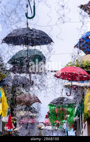 Kunstwerke aus Dutzenden von mehrfarbigen Regenschirmen, die über einer Straße in Camara de Lobos, Madeira, hängen. Stockfoto