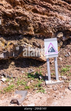 Ein Schild warnt vor der Gefahr, dass Steine von einer instabilen Klippe fallen. Stockfoto