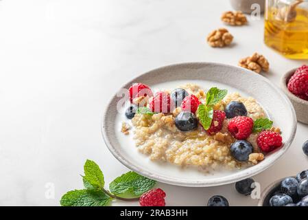 Quinoa-Haferbrei mit frischen Heidelbeeren, Himbeeren, Walnüssen und Minze in einer Schüssel auf weißem Hintergrund. Schließen Stockfoto