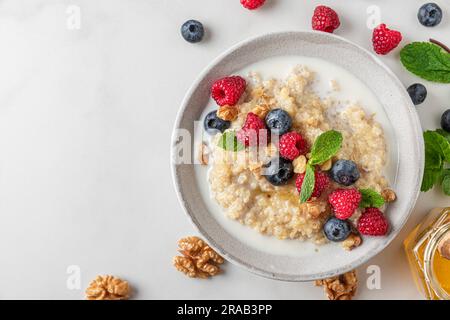 Gesundes Frühstück. Quinoa-Haferbrei mit frischen Beeren, Nüssen und Minze in einer Schüssel auf weißem Hintergrund. Draufsicht Stockfoto