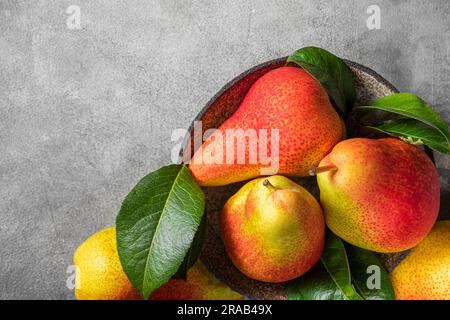 Birnenfrüchte mit grünen Blättern in einer Schüssel auf grauem Hintergrund. Draufsicht mit Kopierbereich Stockfoto
