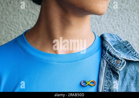 Teenager-Junge mit Autismus-Unendlichkeits-Regenbogen-Symbol auf T-Shirt mit metallischer Brosche. Welttag des Autismus-Bewusstseins, Autismus-Rechte-Bewegung Stockfoto