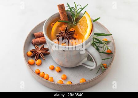 Eine Tasse Sanddorntee mit Orangen, Beeren, Zimt und Rosmarin auf einem weißen Tisch. Schließen. Gesundes Kräutergetränk Stockfoto