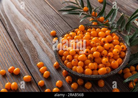 Frische, reife Sanddornbeeren im Herbst mit Blättern auf Holzhintergrund. Schließen Stockfoto