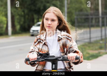 Junge Frau auf einem elektrischen Roller fährt die Straße runter Stockfoto