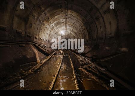 Dunkel dreckiger verlassener U-Bahn-Tunnel mit rostigen Eisenbahnen Stockfoto