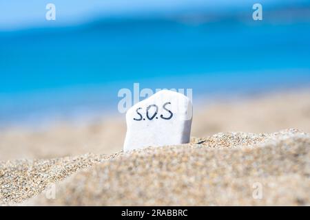 SOS - das Wort, das auf einem Stein im Sand am Strand vor dem Hintergrund des türkisfarbenen Meeres zeichnet. Hilfe! Hilfe! Rette den Ozean. Ökologie und Umwelt Stockfoto