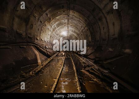 Dunkel dreckiger verlassener U-Bahn-Tunnel mit rostigen Eisenbahnen Stockfoto