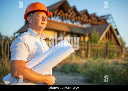 Junger Ingenieur in einem gelben Helm mit Bauplänen auf einer Baustelle Stockfoto