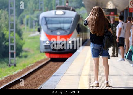 Leute, die auf den ankommenden Zug am Bahnhof warten. Pendlerzugpassagiere im Sommer Stockfoto