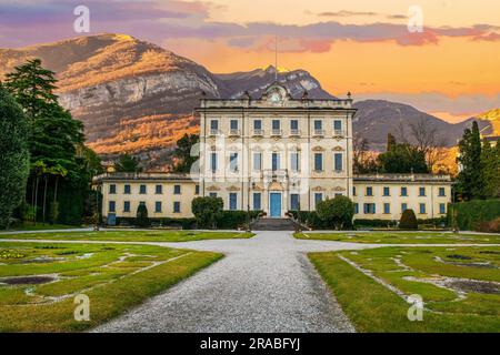 Alte Villa Sola Cabiati in Tremezzo, am Comer See. Lombardei, Italien. Erstaunliche Berg Hintergrund in gelben Strahlen des Sonnenuntergangs Stockfoto