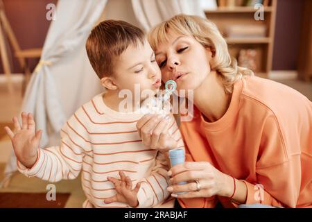 Porträt von Mutter und Sohn mit Down-Syndrom, das beim Spielen zu Hause Blasen bläst Stockfoto