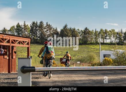 Drei Leute auf Fahrrädern rosten durch und elektronischen eine Barriere, die in die Ferne fuhr Stockfoto