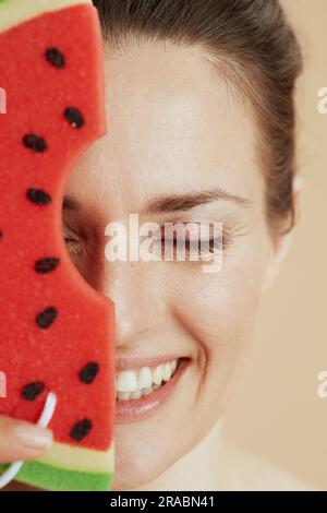 Lächelnde moderne Frau mittleren Alters mit Wassermelonen-Duschschwamm. Stockfoto