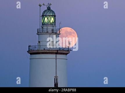 Malaga, Spanien. 02. Juli 2023. Der Buckmond, der am Himmel über einem Leuchtturm aufgeht, ist im Hafen von Malaga zu sehen. Anfang Juli findet der Vollmond der Hirsche als eines der beeindruckendsten astronomischen Ereignisse des Monats statt. Wenn der Vollmond stattfindet, erscheint er größer und heller als normal. (Foto: Jesus Merida/SOPA Images/Sipa USA) Guthaben: SIPA USA/Alamy Live News Stockfoto