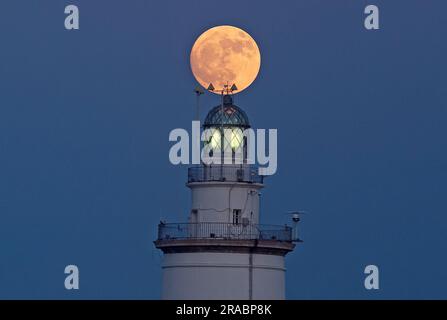 Malaga, Spanien. 02. Juli 2023. Der Buckmond, der am Himmel über einem Leuchtturm aufgeht, ist im Hafen von Malaga zu sehen. Anfang Juli findet der Vollmond der Hirsche als eines der beeindruckendsten astronomischen Ereignisse des Monats statt. Wenn der Vollmond stattfindet, erscheint er größer und heller als normal. (Foto: Jesus Merida/SOPA Images/Sipa USA) Guthaben: SIPA USA/Alamy Live News Stockfoto