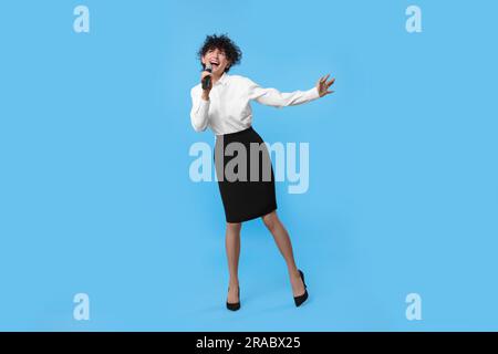 Wunderschöne junge Frau mit Mikrofon, das auf hellblauem Hintergrund singt Stockfoto