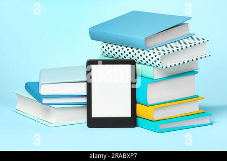 Moderner E-Book-Leser und Stapel von Hardcover-Büchern auf hellblauem Hintergrund Stockfoto