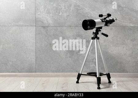 Stativ mit modernem Teleskop nahe der grauen Wand. Platz für Text Stockfoto