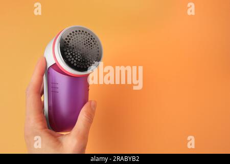 Eine Frau hält einen modernen Rasierer mit Stoff auf blassorangefarbenem Hintergrund, Nahaufnahme. Platz für Text Stockfoto
