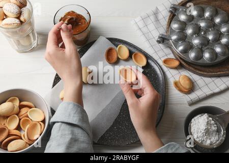 Frau, die leckere walnussförmige Kekse am weißen Holztisch macht, Draufsicht Stockfoto